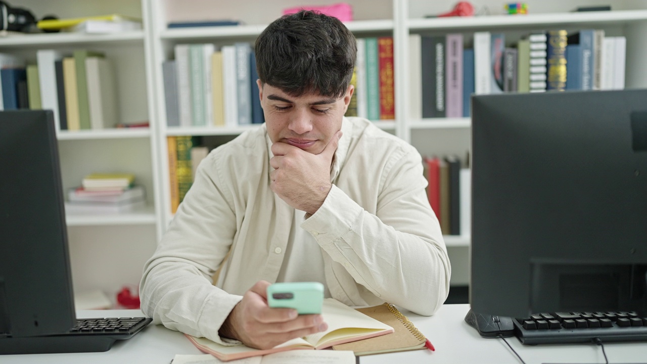 年轻的西班牙裔学生坐在图书馆大学的桌子上使用智能手机视频素材