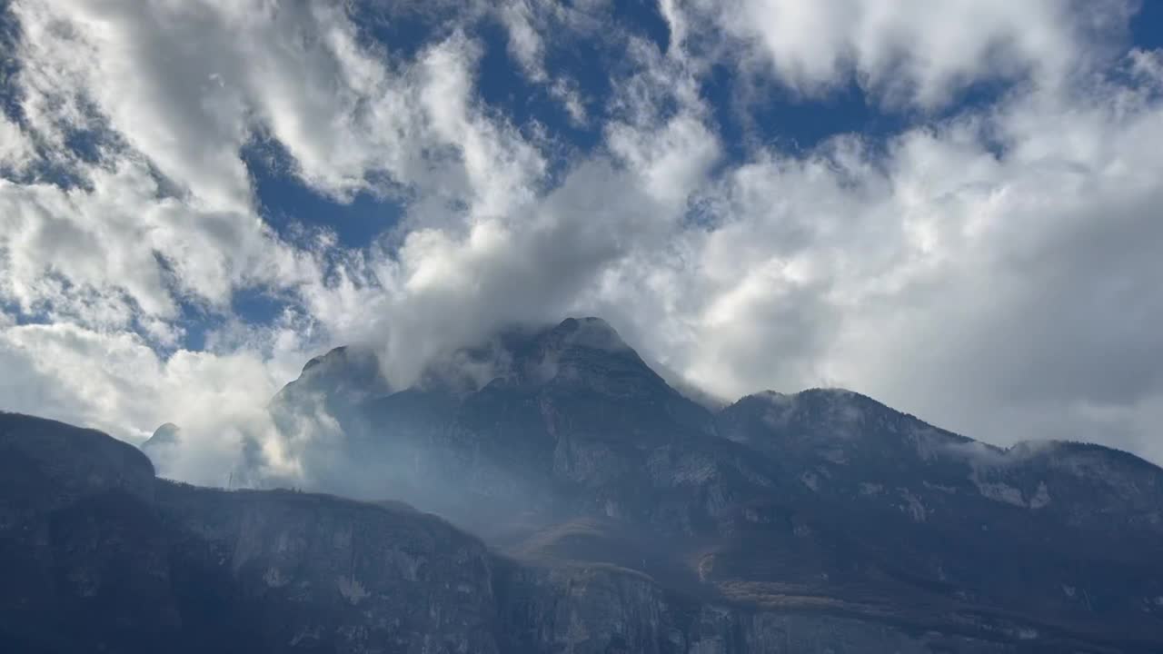 低垂的云层穿过巍峨的群山，映衬着多云的蓝天视频素材