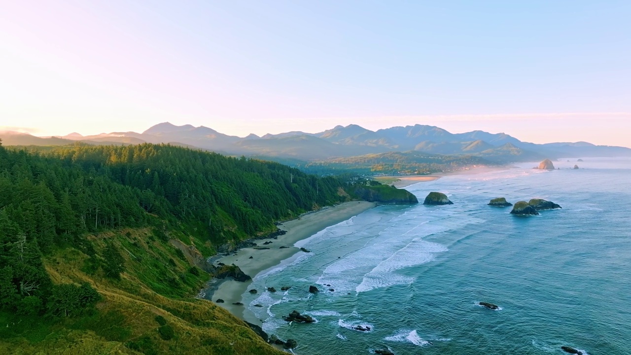 在一个美丽的蓝天夏日，俄勒冈海岸的新月海滩，鸟岩，干草堆岩石和大炮海滩的黄金时间日出跟踪拍摄，远处的山脉。视频素材