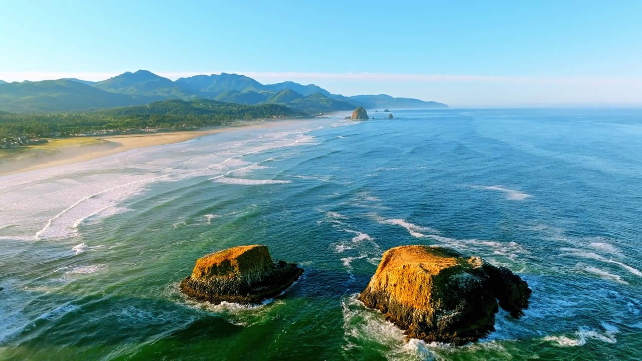 在黄金时间的空中盘旋在海洋上，向右倾斜，显示海浪撞击巨大的岩石，白色的泡沫，海鸥大炮海滩和干草堆岩石视频下载