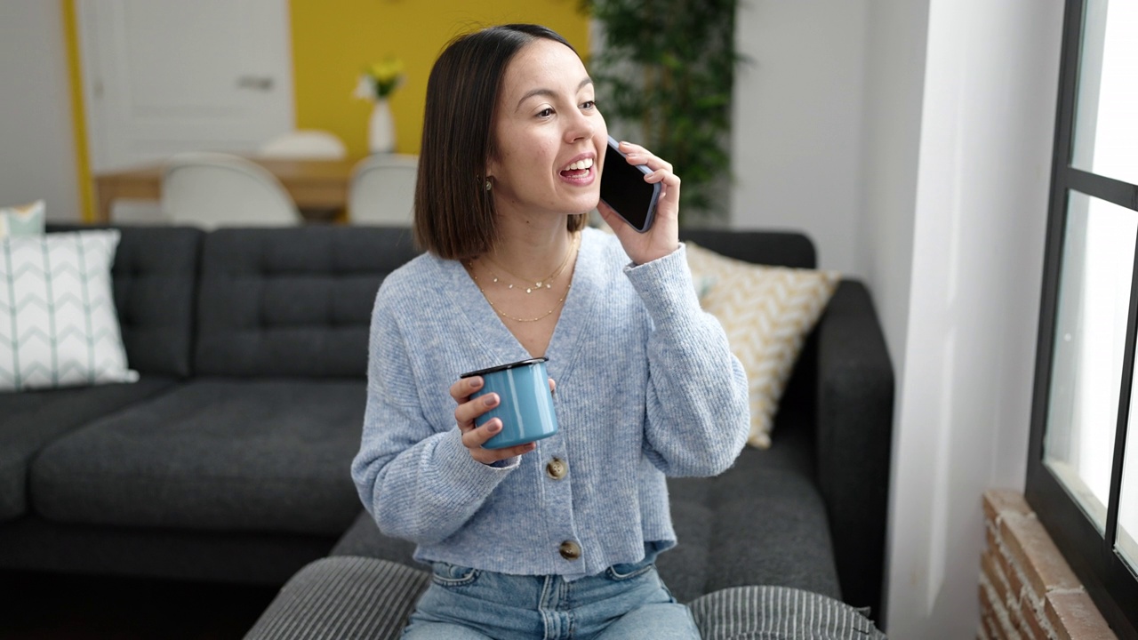 年轻漂亮的西班牙女人在家里用智能手机聊天喝咖啡视频素材