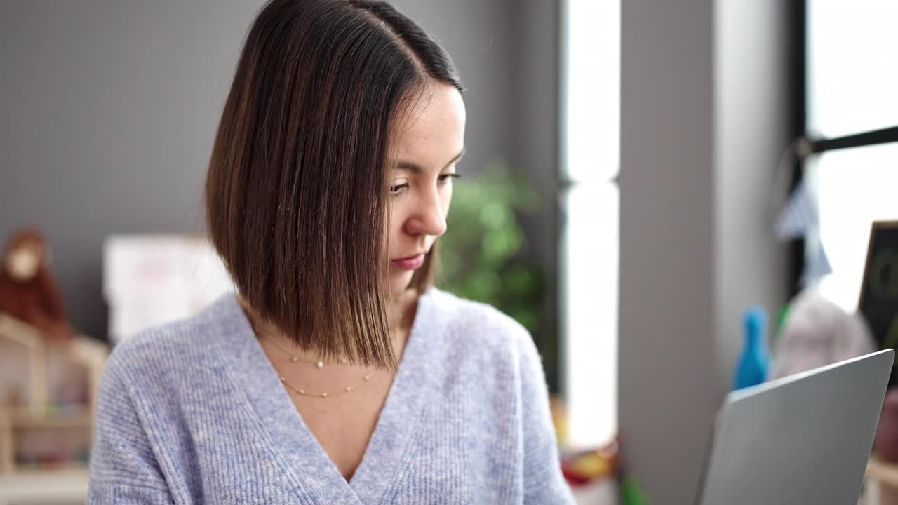 年轻漂亮的西班牙裔女性在幼儿园用笔记本电脑当老师视频素材