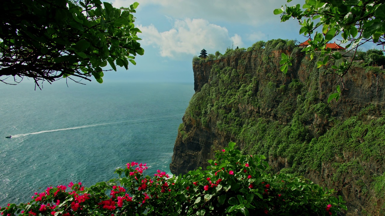 阴天晴朗的印尼巴厘岛，Pura Luhur Uluwatu寺庙的海景。美丽的巨大悬崖上有异国情调的植物，红色品红的花朵映衬着蓝色的印度海水。著名的历史遗迹。视频素材