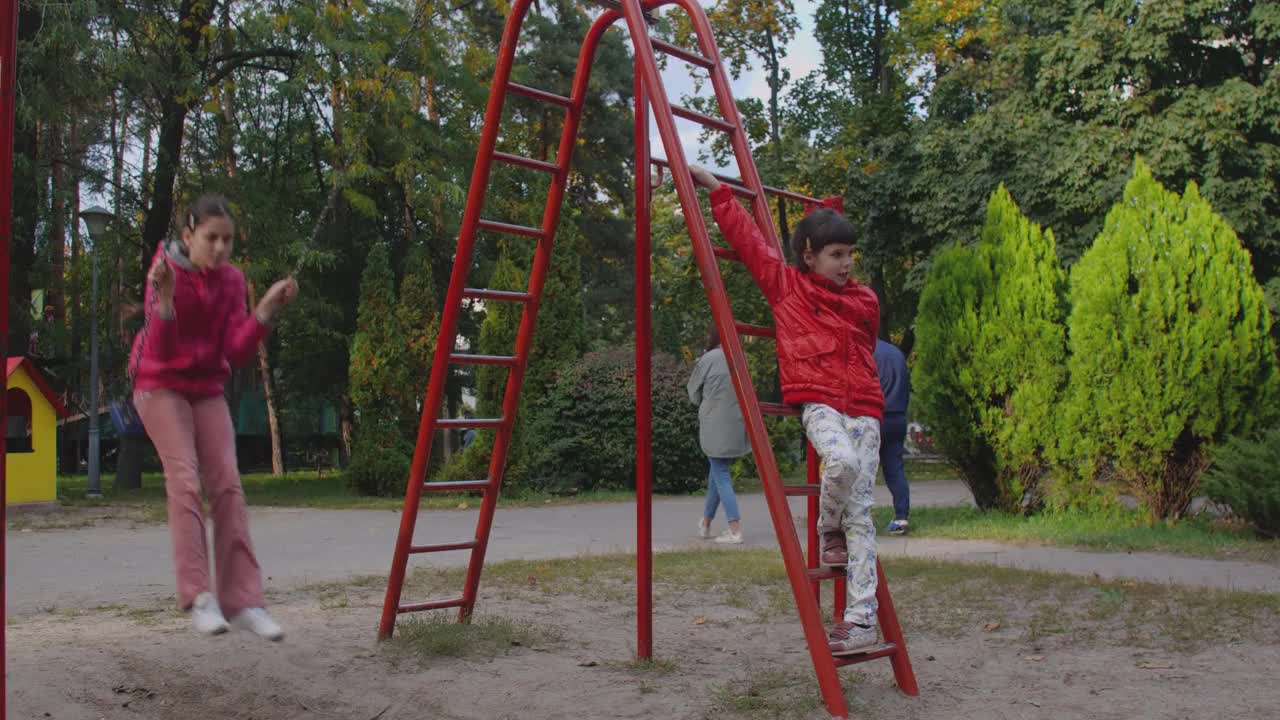 两个漂亮的小姐妹在操场上玩耍，孩子们在温暖的秋日里荡秋千，家庭在城市公园休闲50帧视频下载