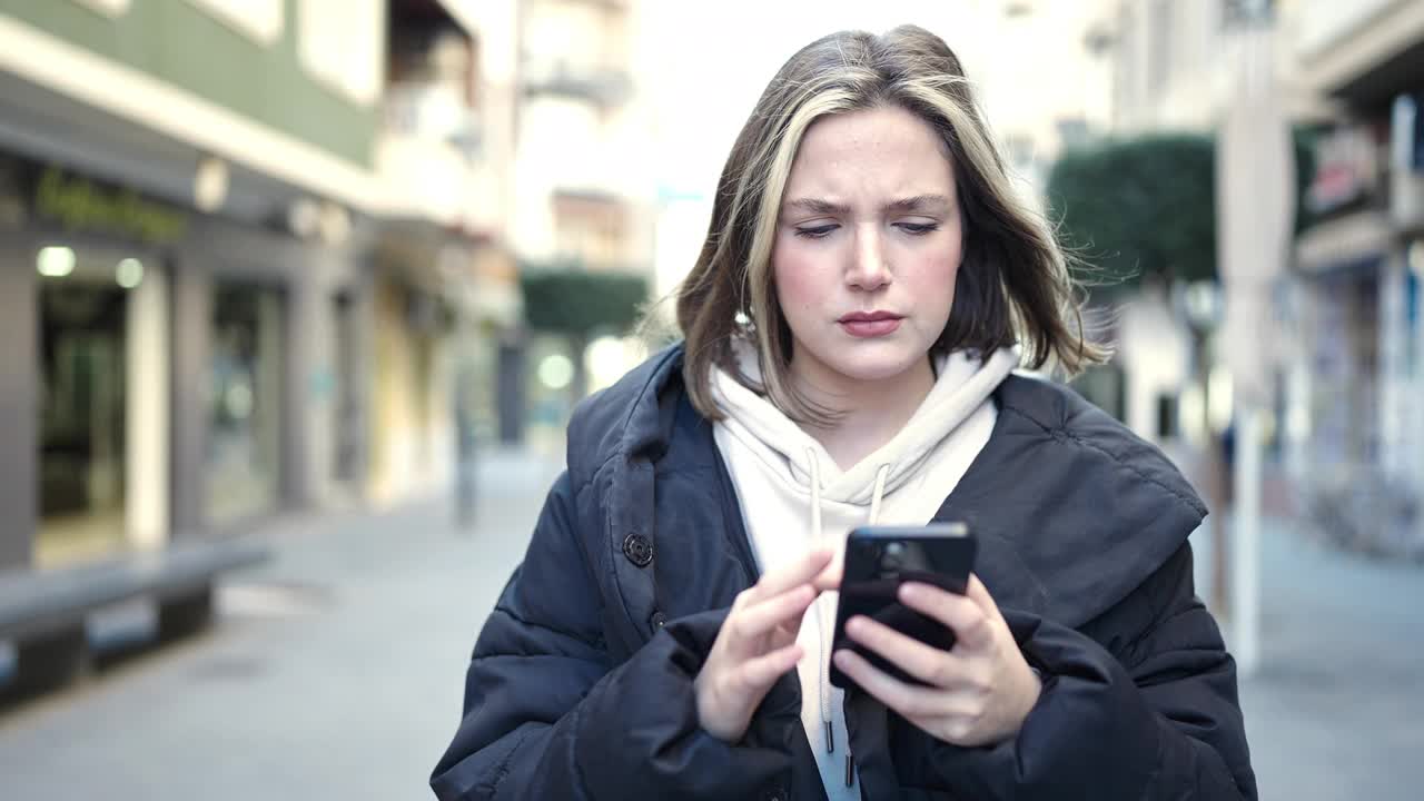 年轻的金发女子在街上用着智能手机，表情严肃视频素材