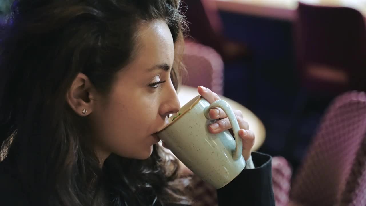 年轻女子在咖啡馆喝茶。快乐的女士在舒适的咖啡馆里休息，喝着薄荷茶。含有抗氧化剂的绿色草药。生活方式的概念。实时视频素材