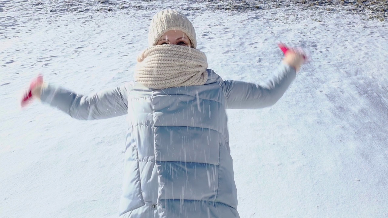 快乐的年轻女子把雪抛向空中，在冬天的雪公园里玩耍视频素材