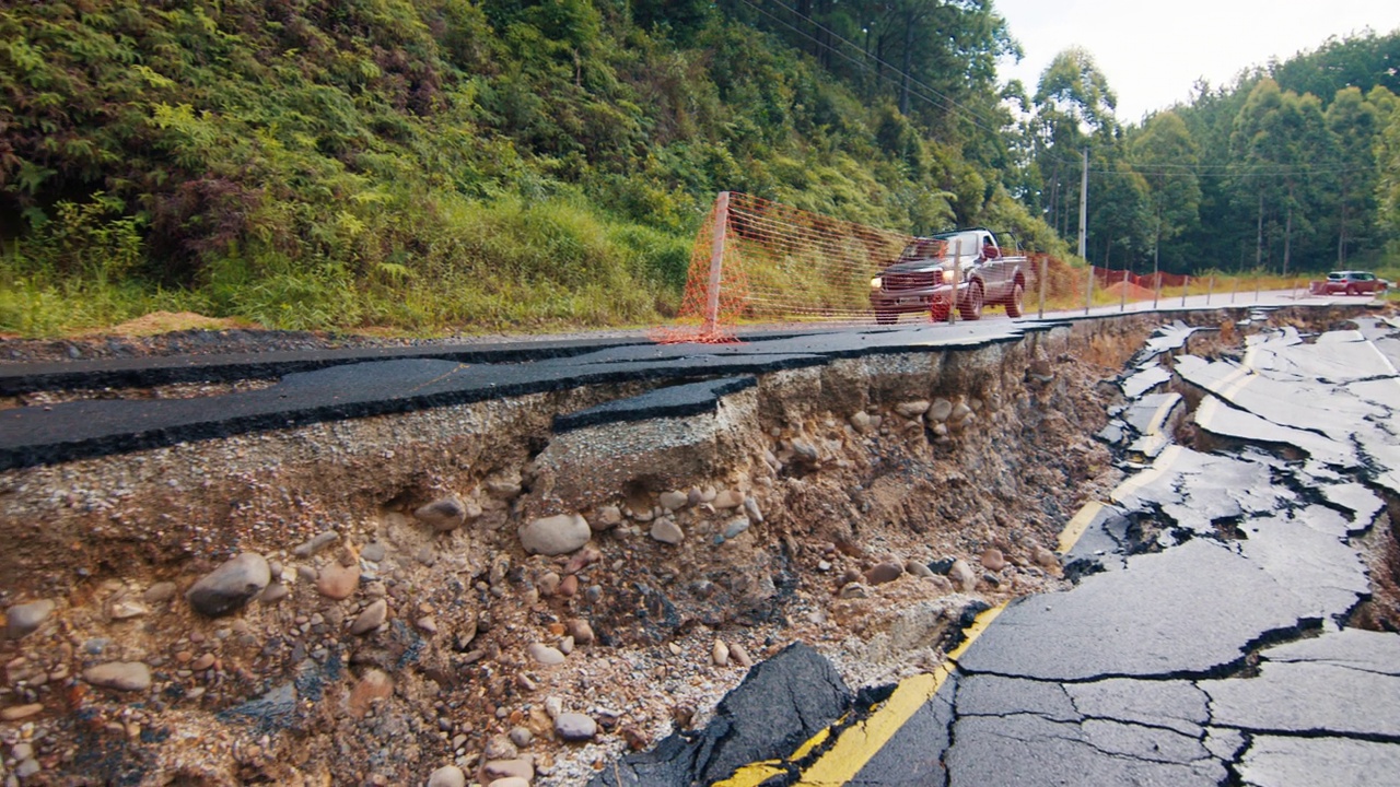 汽车在山间完全损坏的柏油路的车道上行驶。泥石流过后，路面开裂视频素材