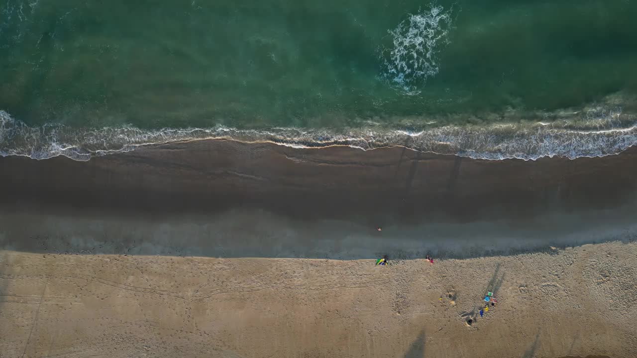 空中俯瞰从冲击海浪在沙滩上夕阳碧绿的海水视频素材