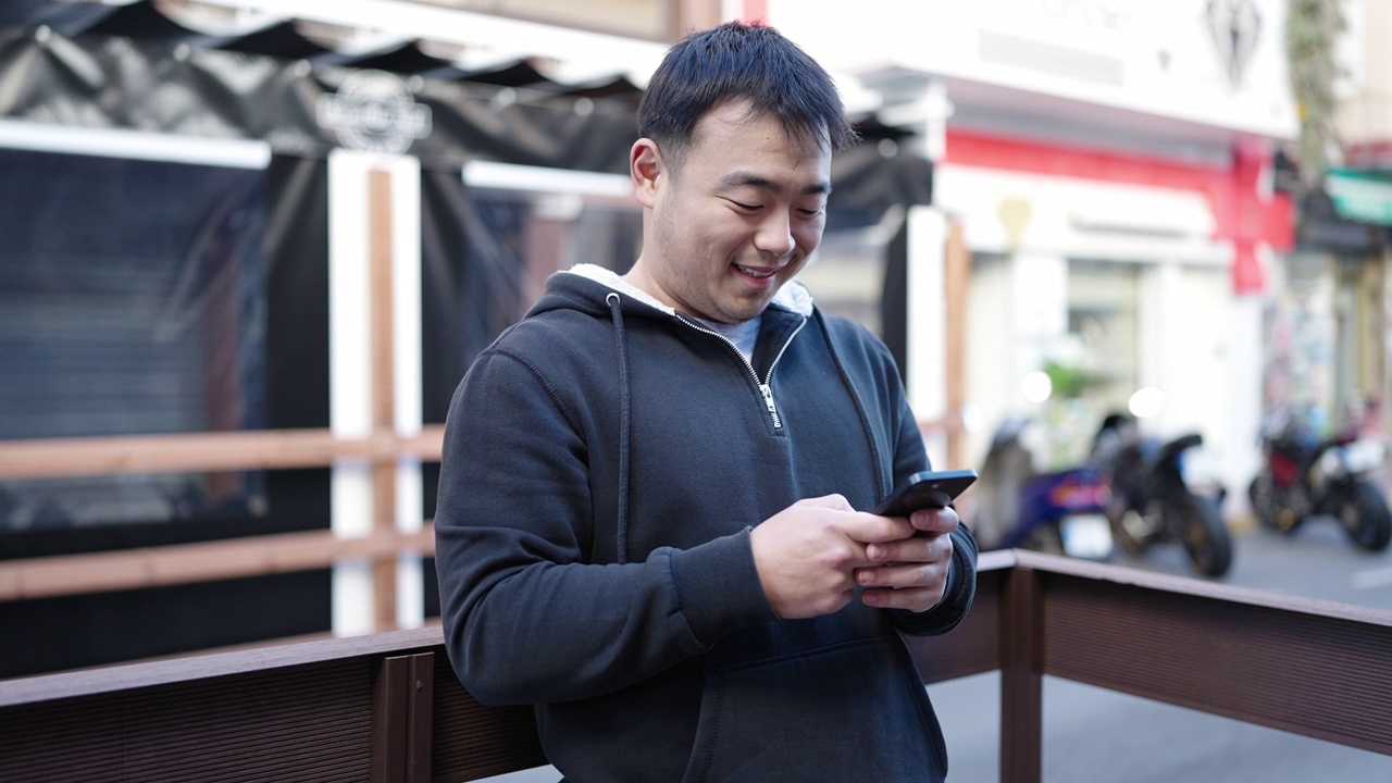 年轻的中国男子在街上用智能手机自信地微笑着视频素材