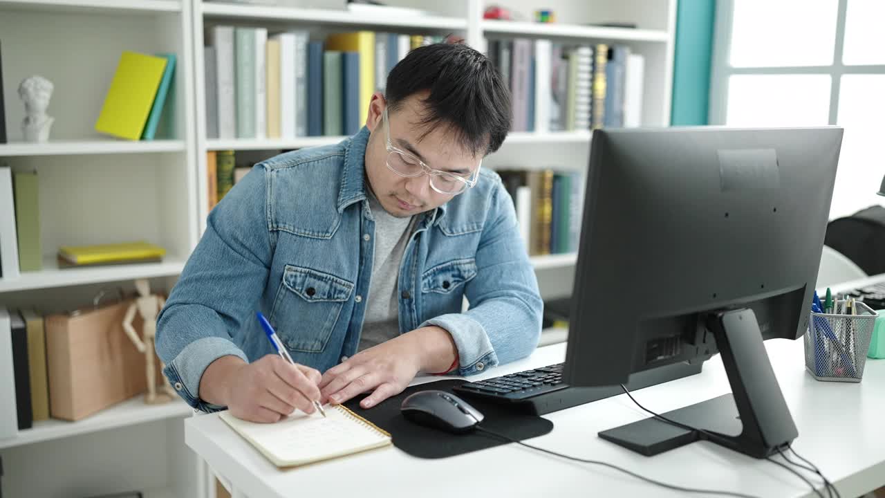 在图书馆大学，年轻的中国男学生正在用电脑在笔记本上写字视频素材