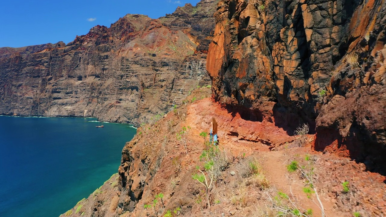 自然景观。一名妇女沿着火山岩走在危险的道路上。蓝色的天空。令人惊叹的海滩。鸟瞰图。旅游目的地。暑假。视频素材