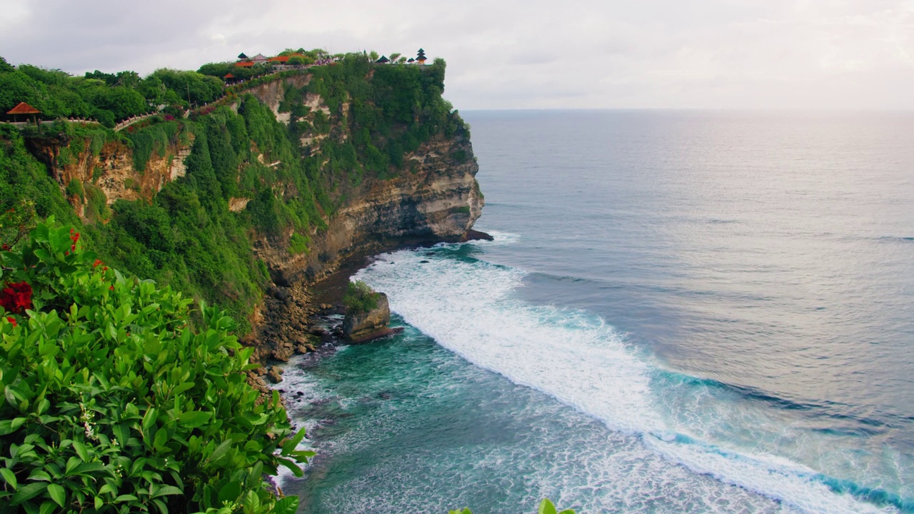 海景与古老的Pura Luhur Uluwatu寺庙巴厘岛印度尼西亚。巨大的悬崖上生长着外来植物，映衬着蓝色的印度海水。著名的历史遗迹。视频素材