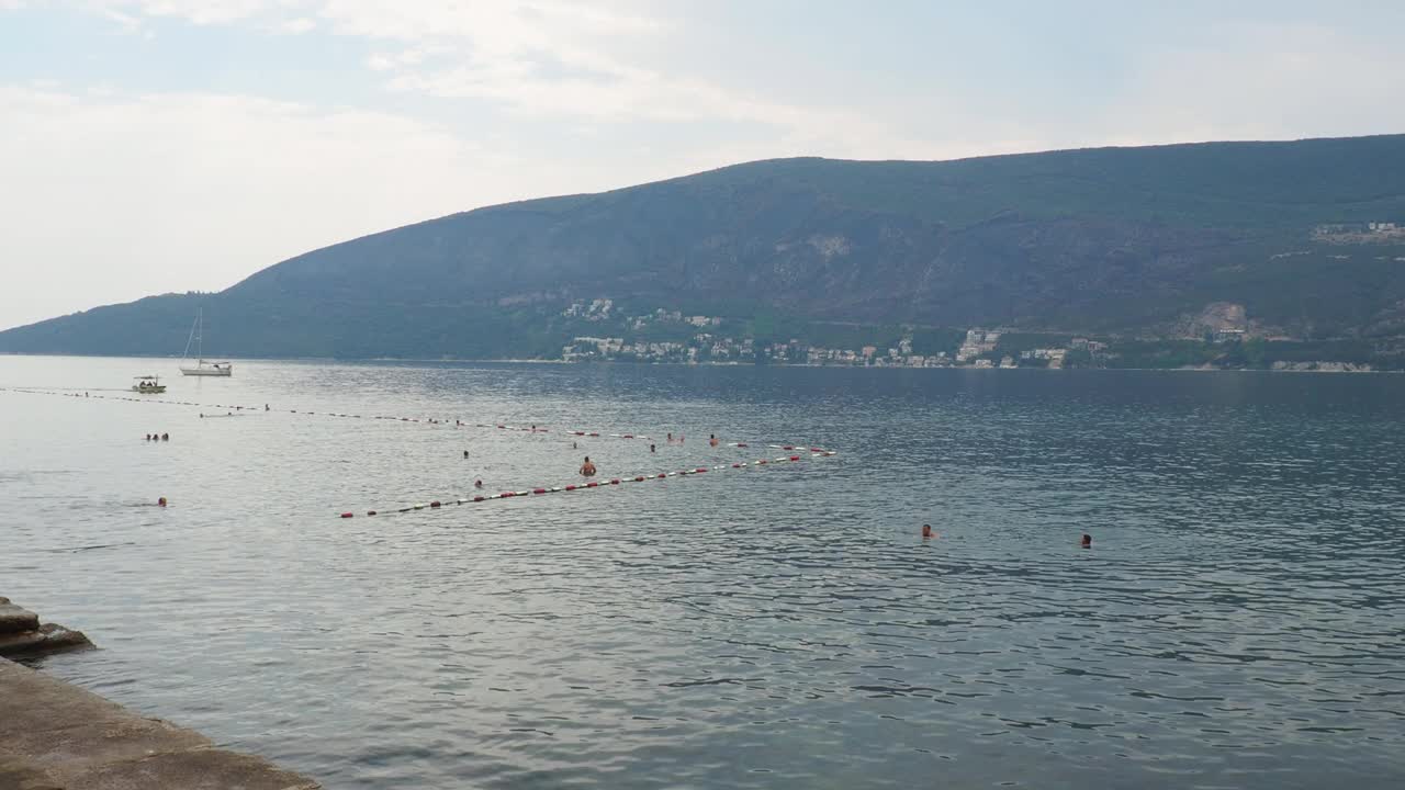 海上度假旅行。小船漂浮在亚得里亚海上。地中海旅行。山峦起伏，水波荡漾。人们游泳，玩得很开心。有浮标限制的游泳区域视频素材