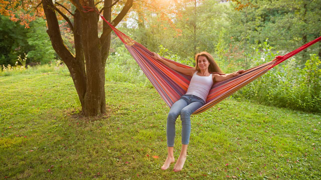 快乐的女人享受夏天，在吊床上荡秋千看日落视频素材