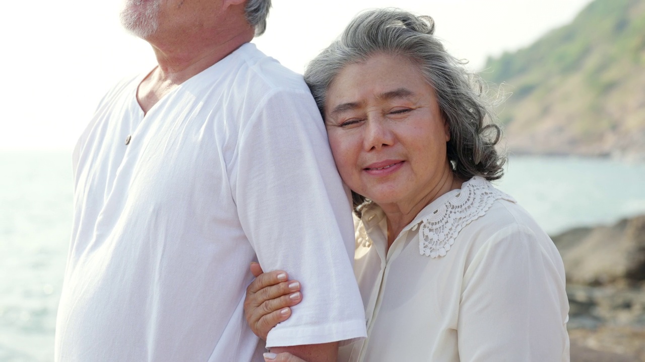 4K亚洲老年夫妇拥抱在悬崖上在夏天的日落。视频素材