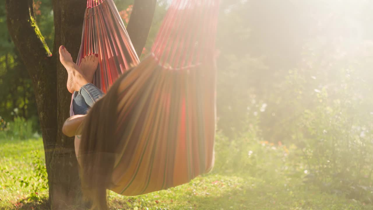 女人享受夏天，在树下的吊床上摇曳视频素材