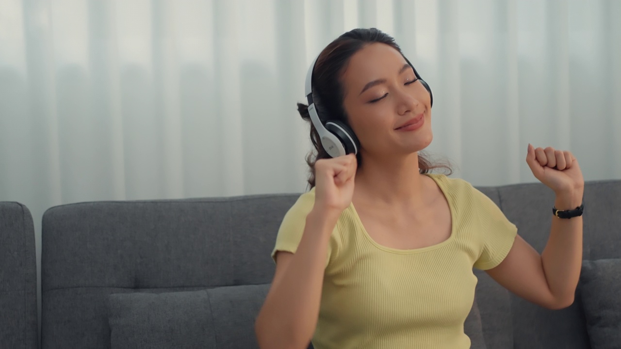 女人戴着耳机，在家里听着音乐，唱着快乐的假期。视频素材