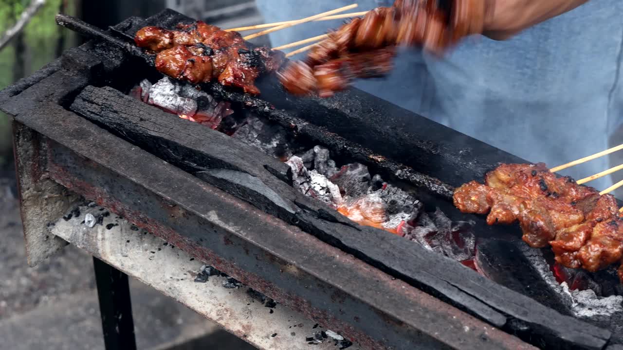 在马来西亚的街头市场摊位上，用传统的木炭烧坑烧烤牛肉和鸡肉沙爹的特写，摊贩翻转和扇火视频下载