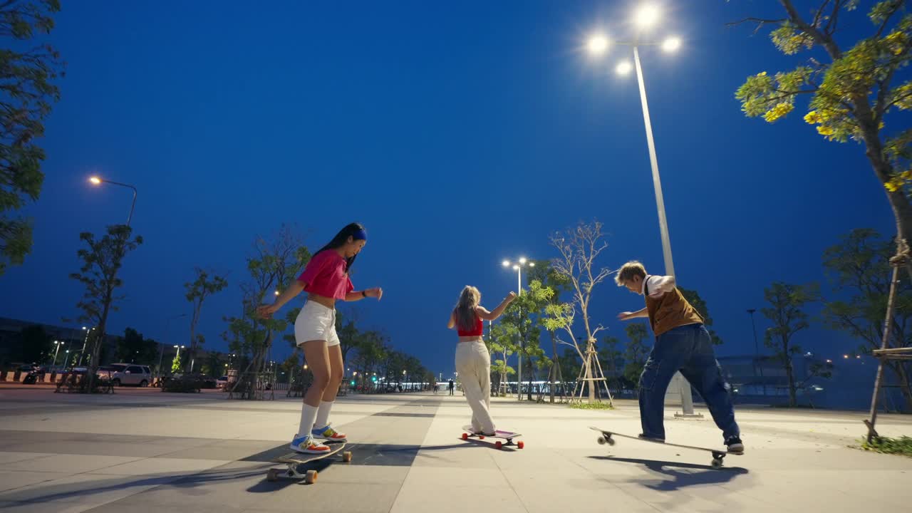 一群亚洲男女在夏夜的公园里滑长板滑板。视频素材