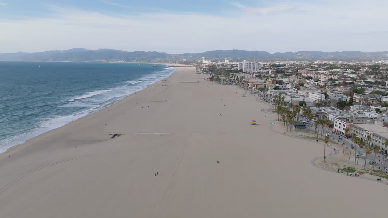 前锋飞越威尼斯海滩。宽阔而空旷的沙滩覆盖着海岸，两旁是棕榈树和建筑。洛杉矶，加利福尼亚，美国视频素材