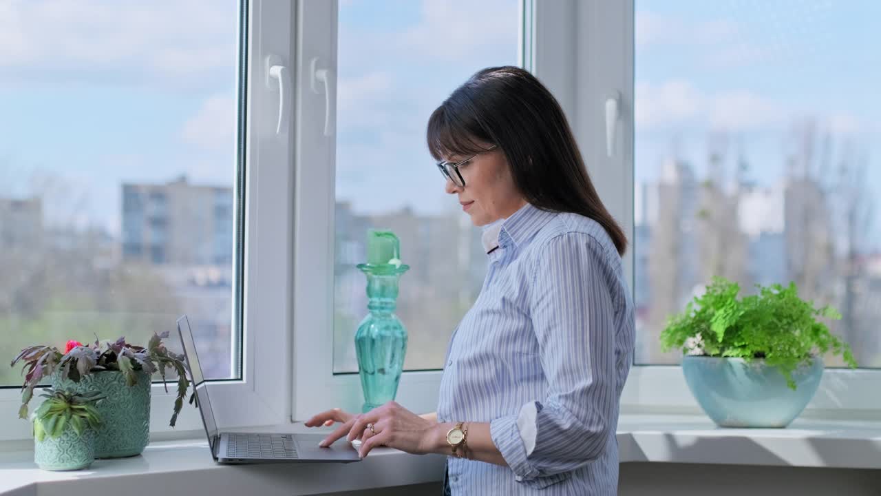 成熟的女人在家里用笔记本电脑打字，全景窗口背景视频素材