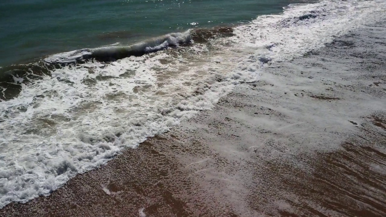 镜头从沙滩移到海浪中，深入到泡沫中。视频素材