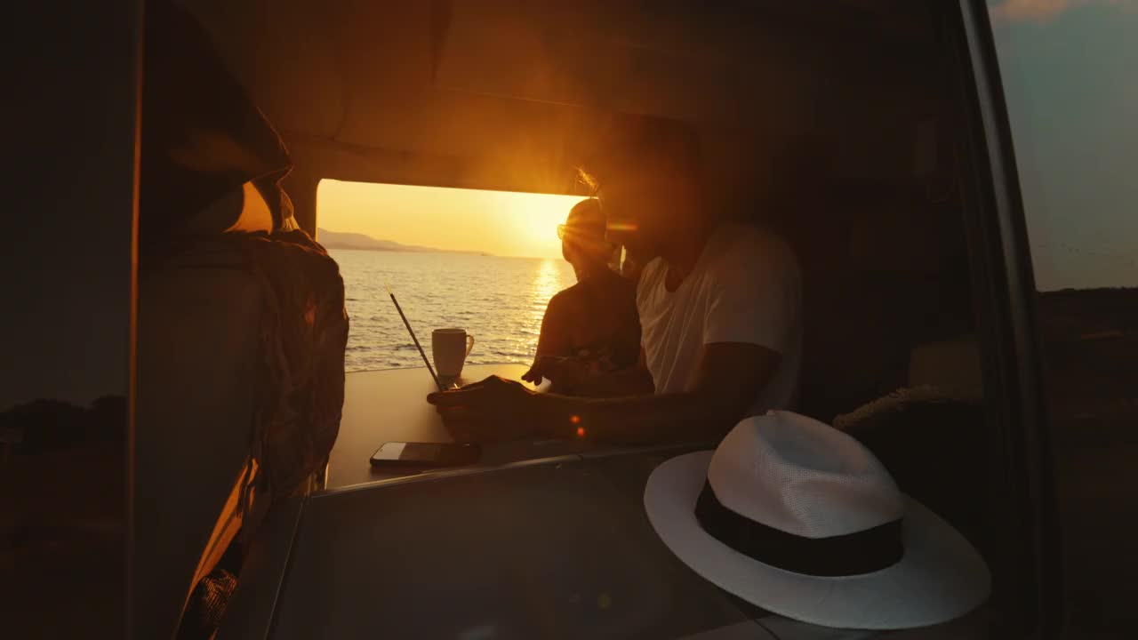 女人在欣赏海景，而她的男朋友在露营车里使用笔记本电脑视频素材