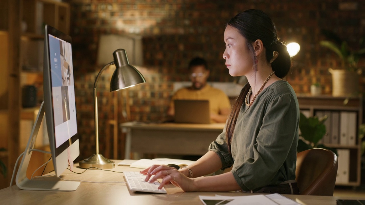 亚洲女性，晚上在办公室电脑上打字，为规划、网页设计和提案截止日期做准备。女性开发人员，在黑暗的工作场所加班，负责网站seo的目标和时间表视频素材