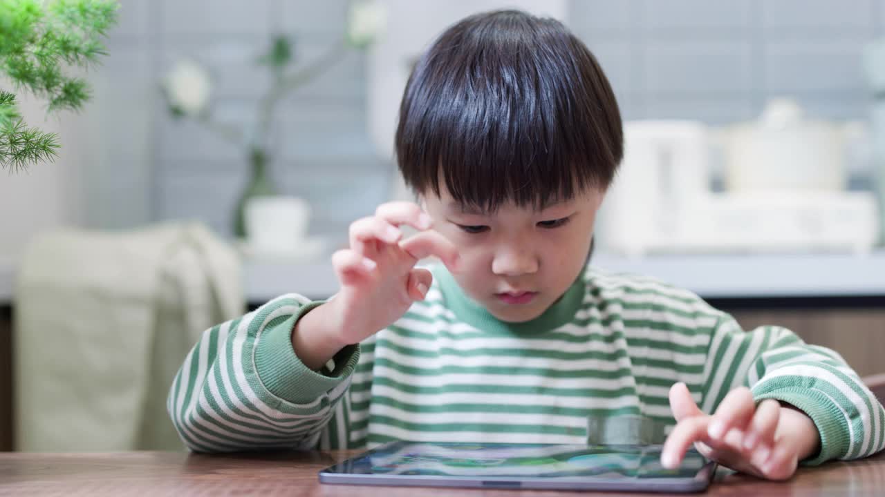 一个小男孩正在餐厅里用电子平板电脑玩游戏视频素材