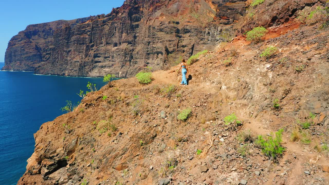 自然景观。一名妇女沿着火山岩走在危险的道路上。蓝色的天空。令人惊叹的海滩。鸟瞰图。旅游目的地。暑假。视频素材