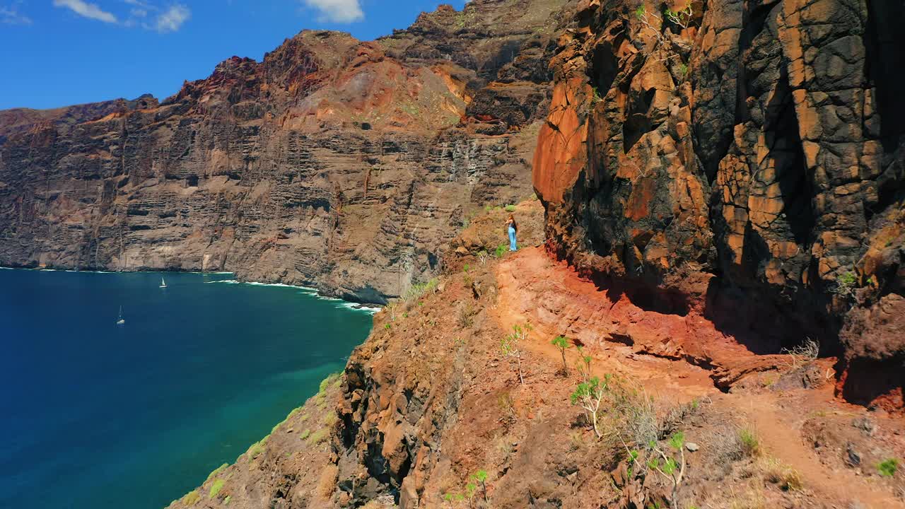 自然景观。女孩喜欢风景。沿着火山岩层的危险道路。蓝色的天空。令人惊叹的深海海滩。鸟瞰图。旅游目的地。加那利岛的特内里费岛视频素材