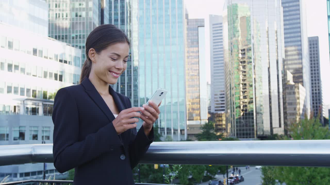 一名女子在温哥华商业区用手机上的应用程序发短信。穿着西装外套使用智能手机的年轻女商人。20多岁的城市女性专业人士。公元前,加拿大。视频素材