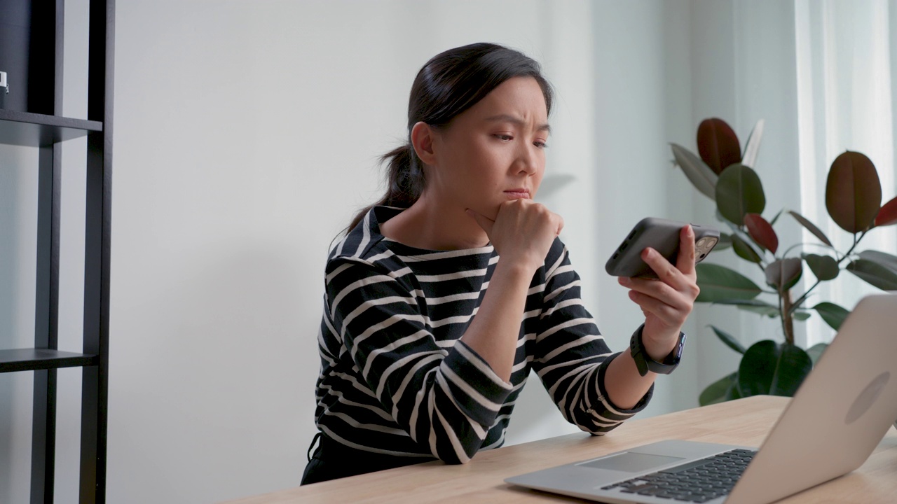 亚洲女性玩电子游戏的智能手机失败，输掉了游戏坐在家里的办公室。视频素材