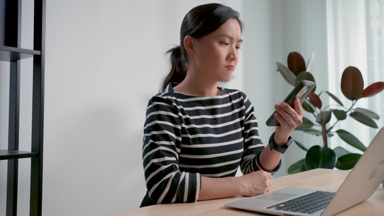 亚洲女性玩电子游戏的智能手机失败，输掉了游戏坐在家里的办公室。视频素材