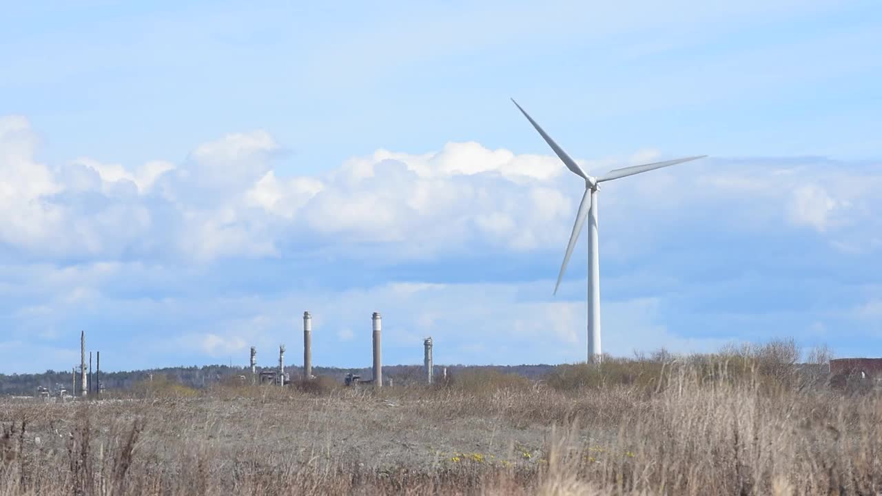 风力涡轮机在强风中旋转，由农田和工业建筑组成视频素材