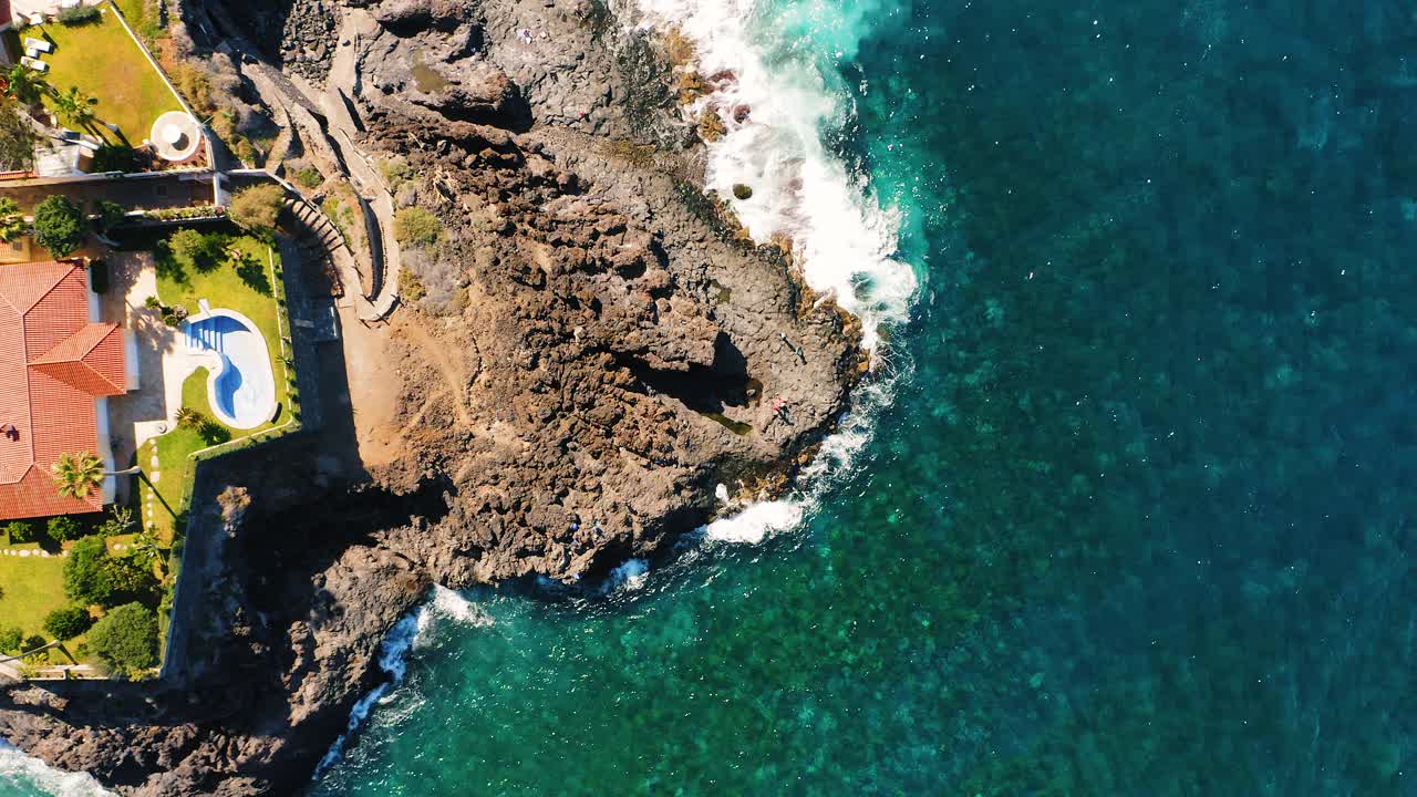 度假小镇海岸线上有岩石海滩，海浪撞击，在热带海岸上有火山形成，石头。阳光明媚的一天。海边，碧蓝碧蓝的海水。鸟瞰图。视频素材