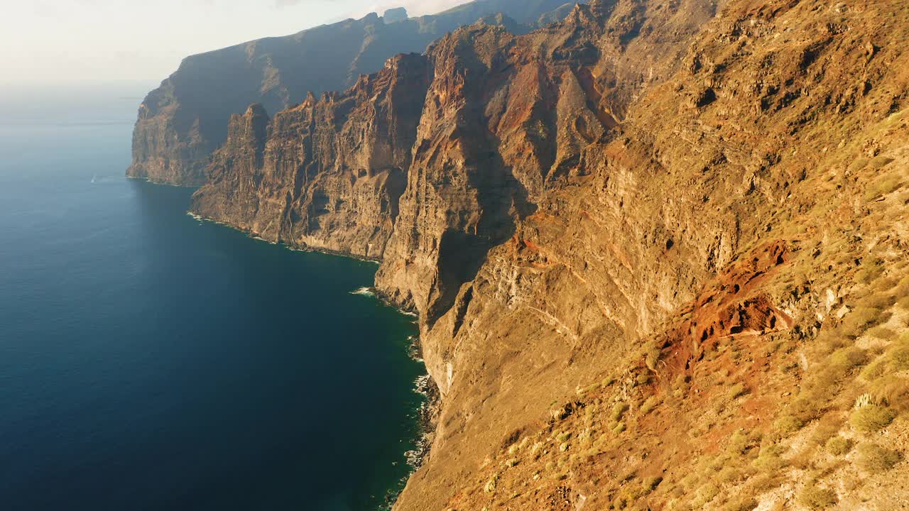 陡峭的悬崖，沙漠火山山脉形成了西班牙加那利群岛特内里费岛的海岸线。Los Gigantes的岩石有着深蓝色的海水。日落时电影般的空中飞行。视频素材