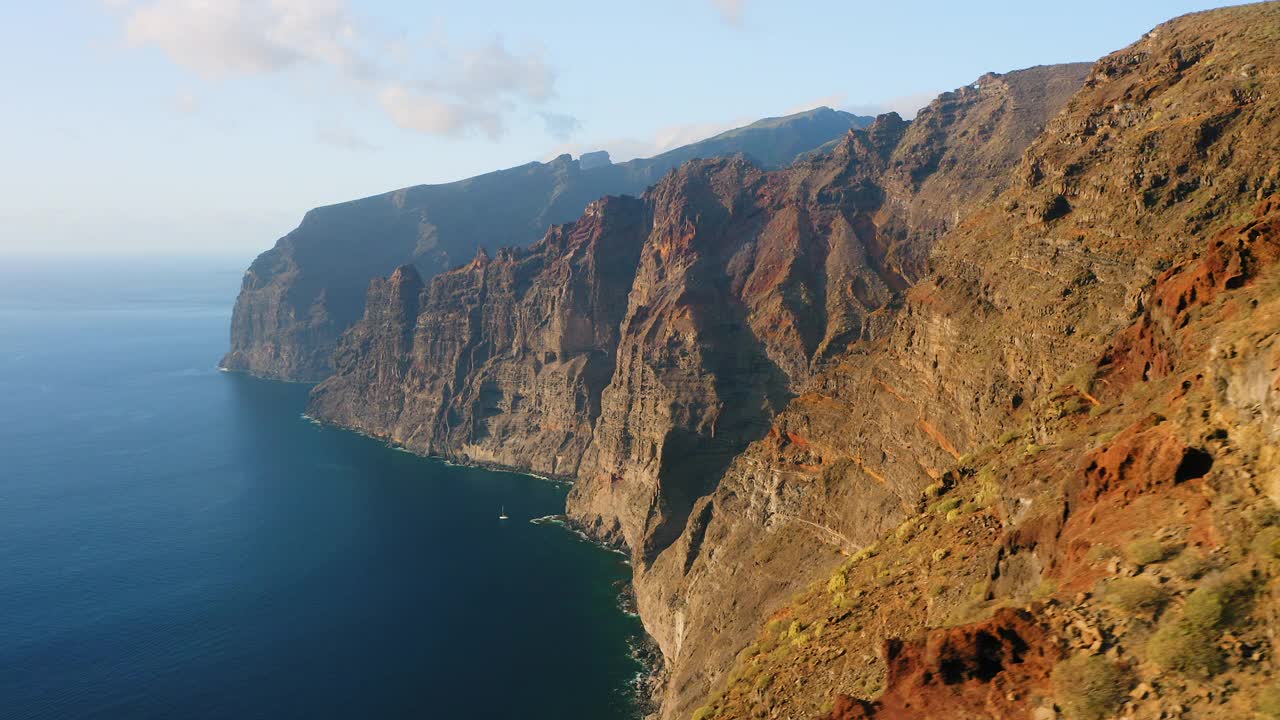 美丽的山崖日落。令人惊叹的空中飞行在深海蓝色的水，棕色和红色的巨大岩石。巨人特内里费岛。环游世界。充满活力的颜色。视频素材