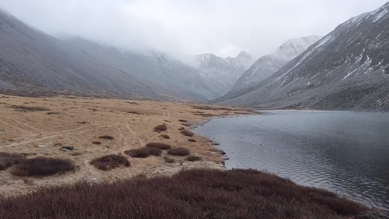 在初冬的雷雨云和飘落的雪下，一个山谷被两座山脉挤压着，还有一个风景如画的湖泊的碎片。视频素材