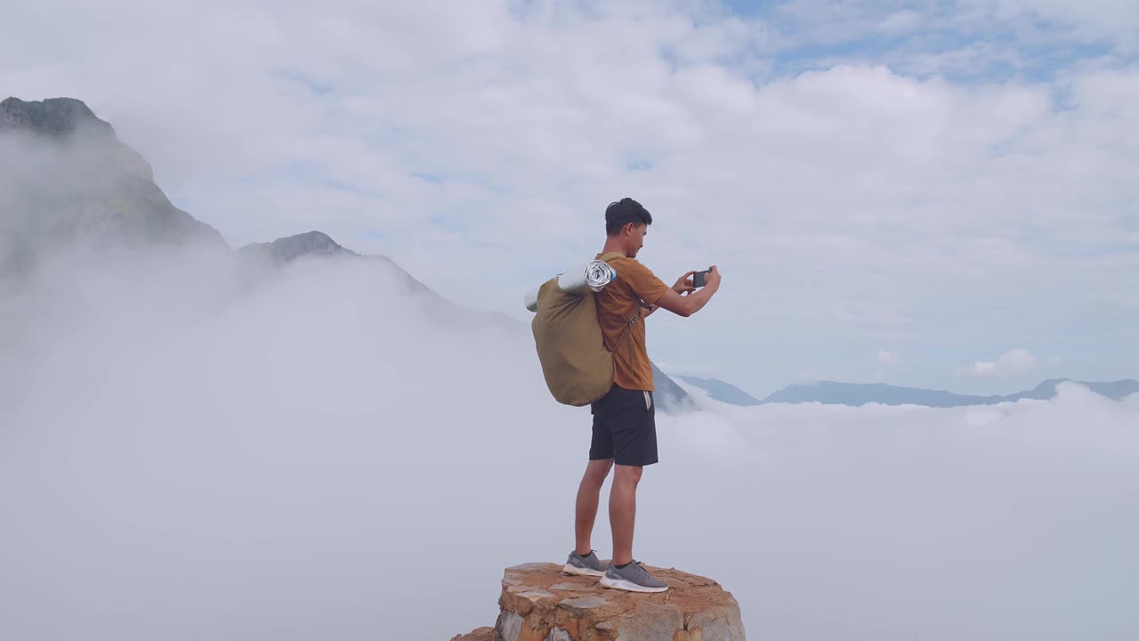 亚洲徒步旅行者站在岩石上，用智能手机拍摄山顶雾山的照片视频素材