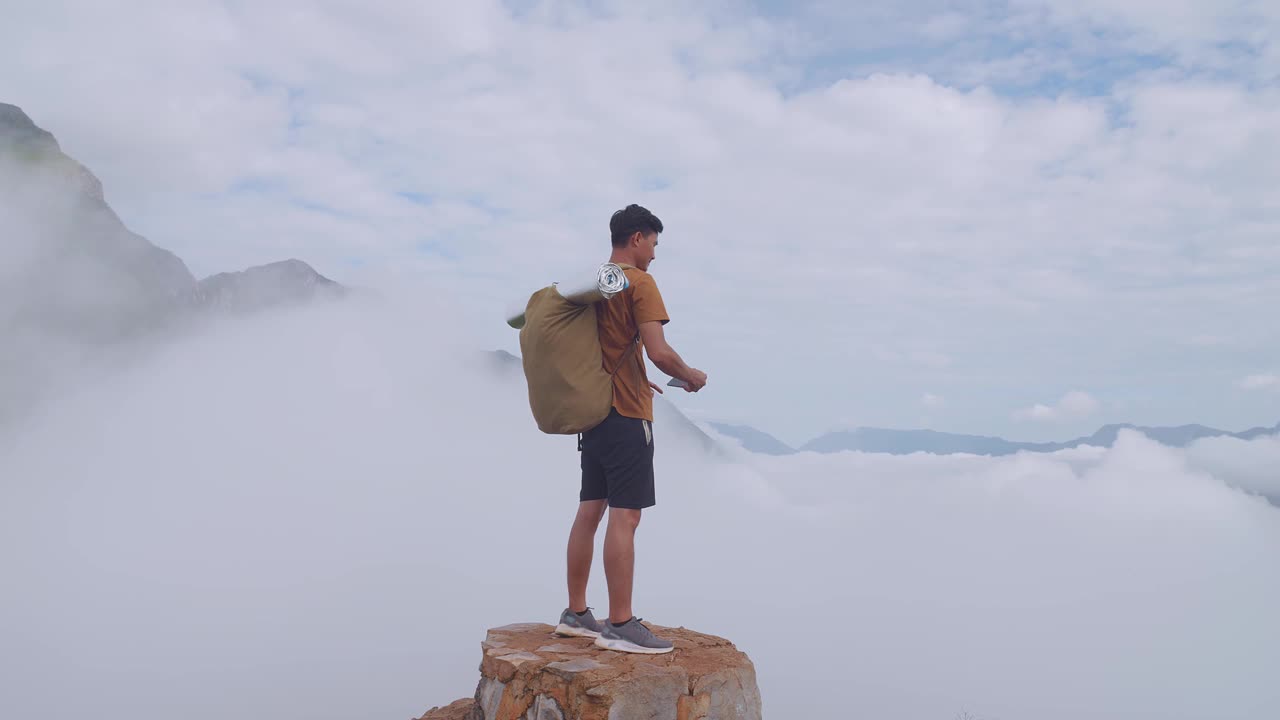 亚洲徒步旅行者站在岩石上，用智能手机拍摄山顶雾山的照片视频素材