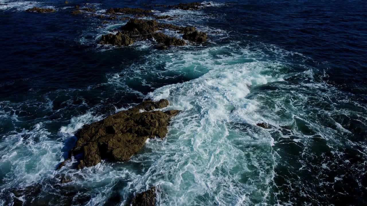 在阳光明媚的日子里，无人机拍摄的海浪拍打着泡沫的岩石悬崖视频素材