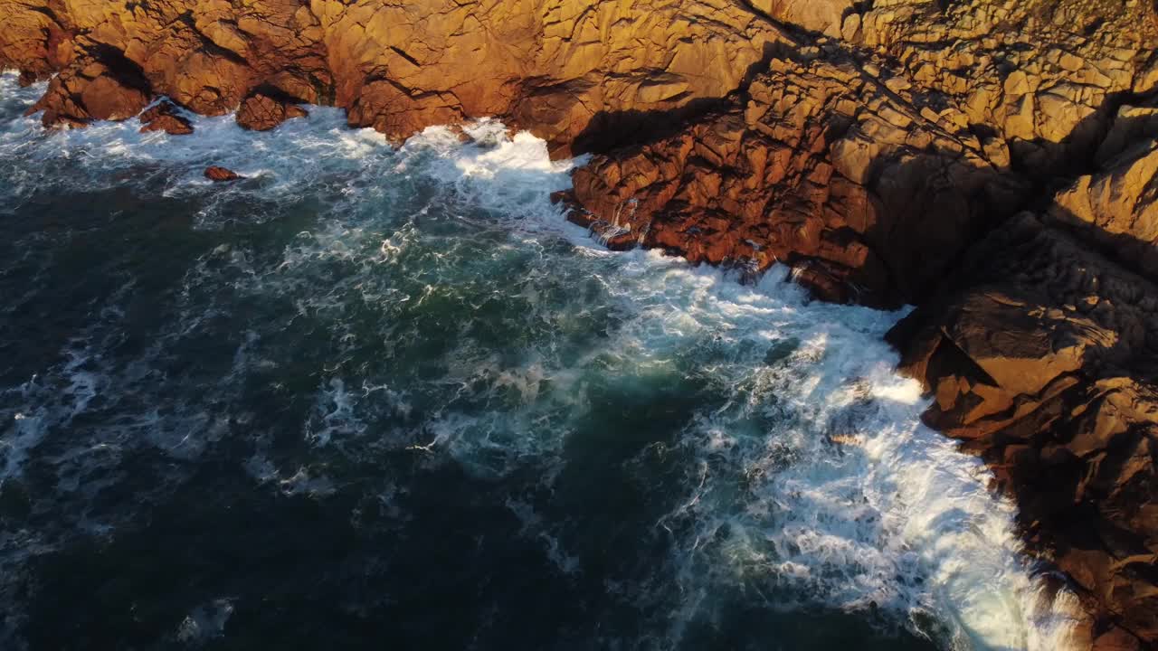 日落时分，无人机拍摄的海浪冲击棕色岩石悬崖的景观视频素材