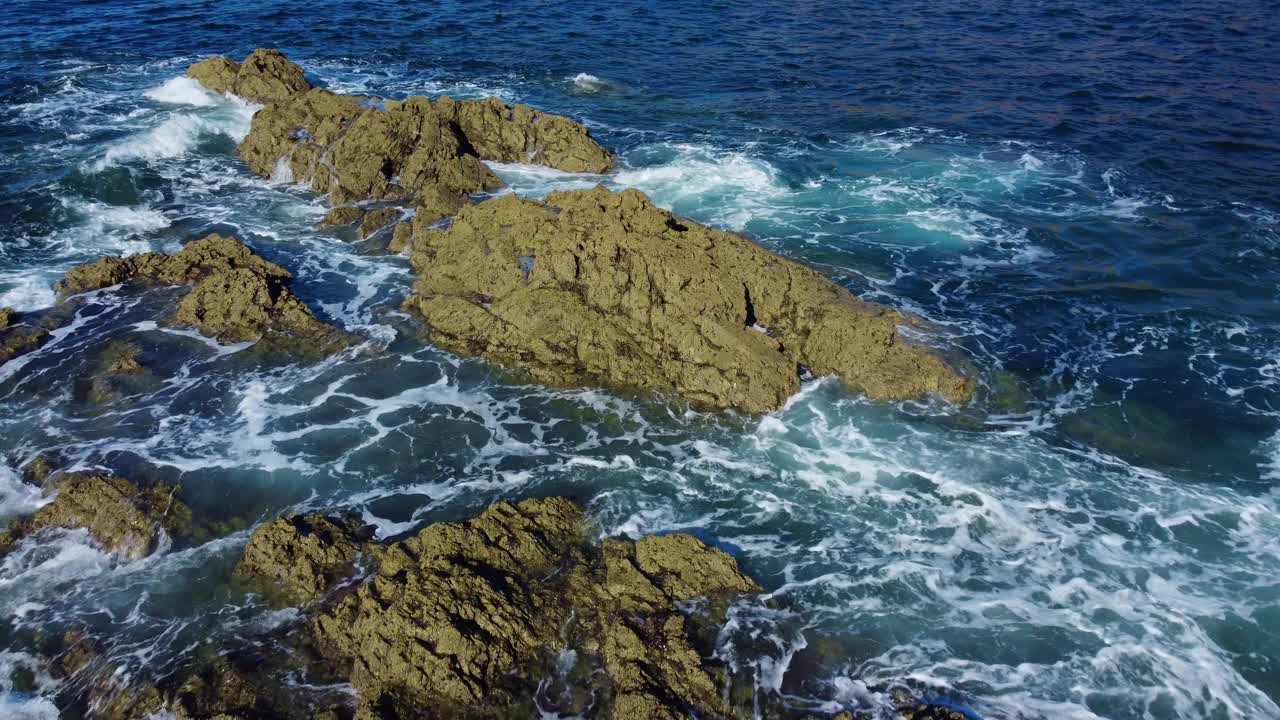 无人机拍摄的海浪打破了岩石悬崖上的泡沫和绿色岩石视频素材