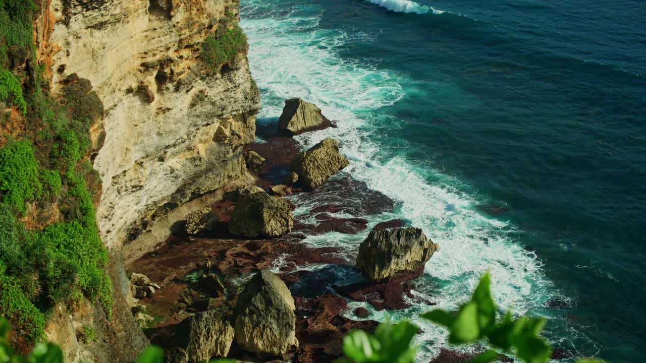 放松海景与绿松石宽泡沫浪滚在岩石悬崖海滩蓝色水晶清澈的水。宁静的禅意绿色自然背景。绿色植物，前景中的热带植物。视频素材