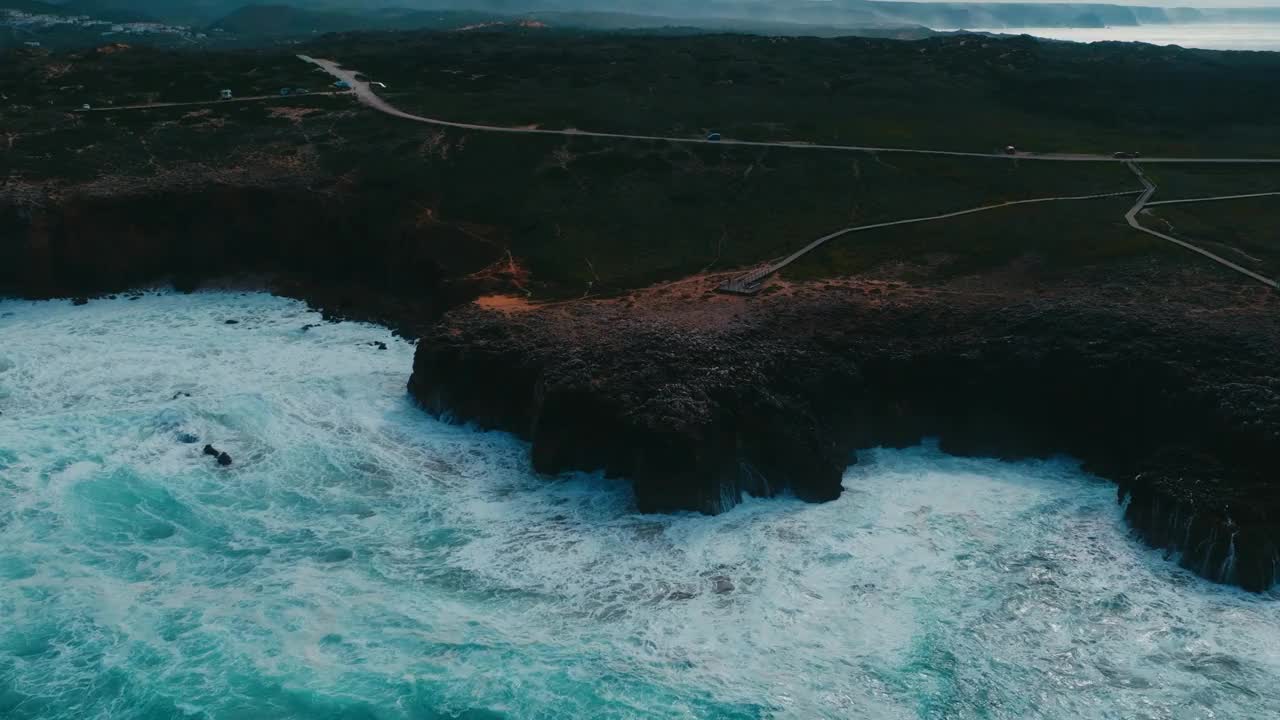 无人机拍摄的海浪飞溅在悬崖岛上，有绿色的草坪和道路视频素材