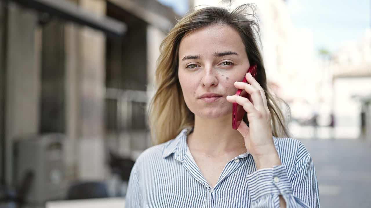 年轻的金发女子在街上用智能手机自信地微笑着视频素材