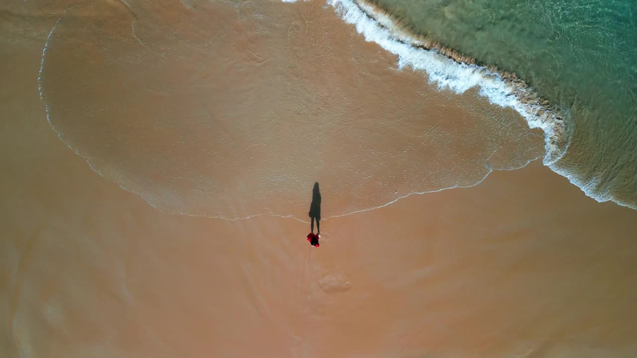 鸟瞰图，穿着红色衣服的女人在海滩上快乐地玩着海浪视频下载