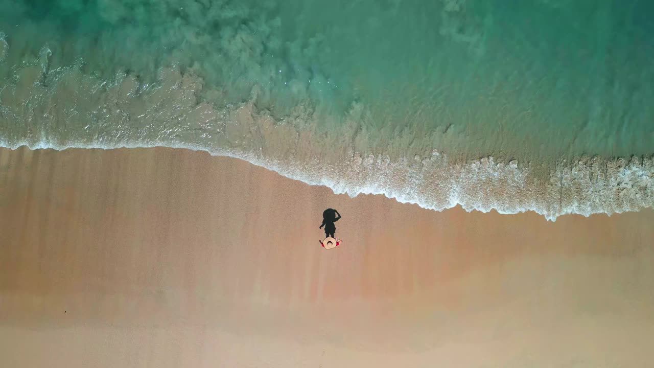 鸟瞰图，穿着红色衣服的女人在海滩上快乐地玩着海浪视频素材